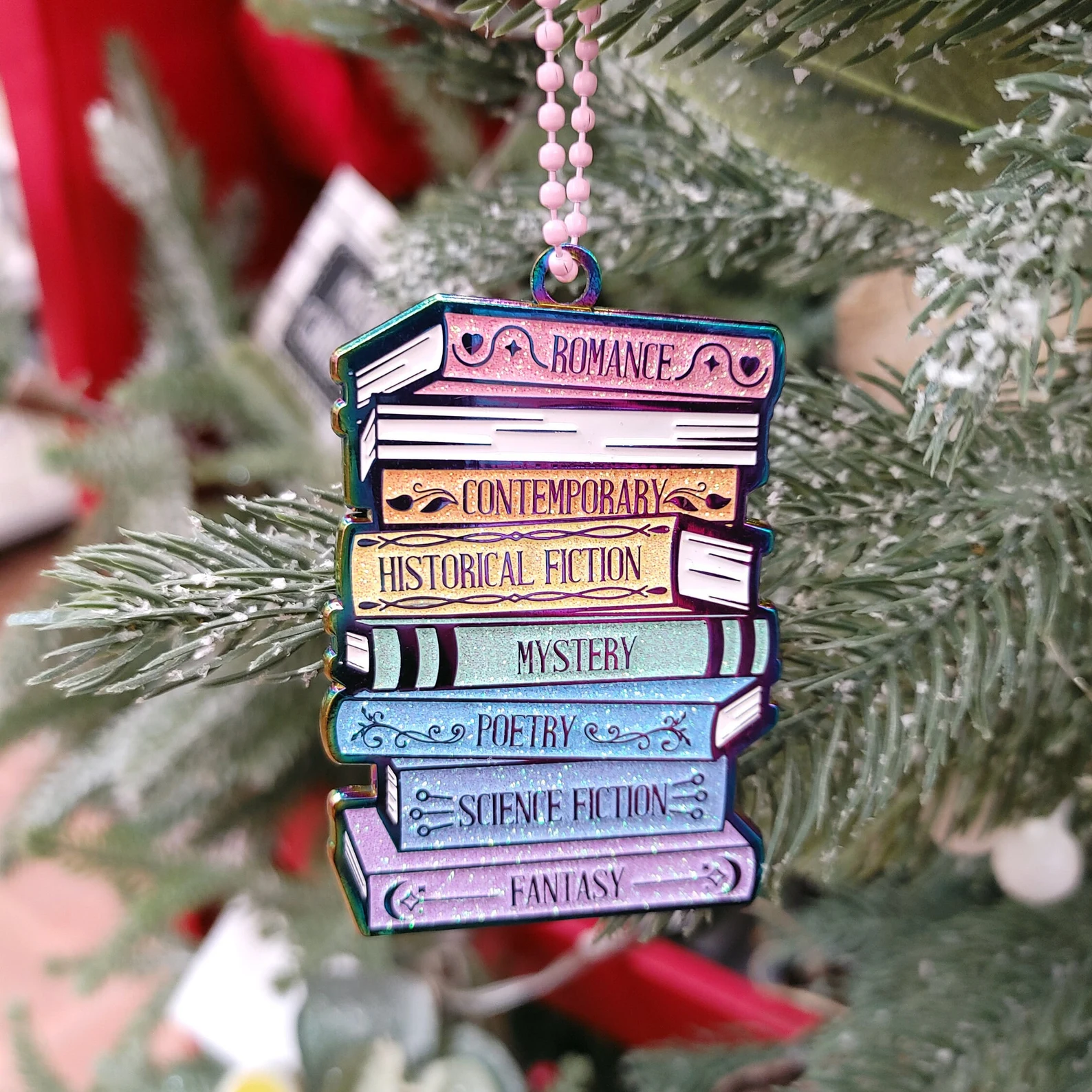 image of an ornament designed like a stack of books. The covers are in rainbow colors with different genres on the spine. 