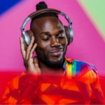 a Black person wearing a rainbow shirt listening to headphones