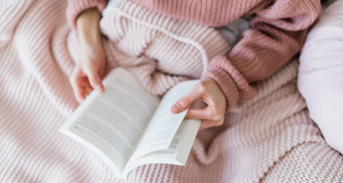 someone wearing a pink sweater reading under a blanket