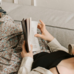 a photo of a person with light skin and a prosthetic leg reading on a couch