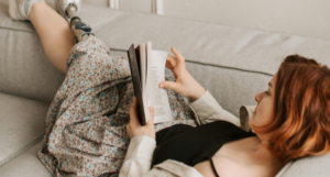 a photo of a person with light skin and a prosthetic leg reading on a couch