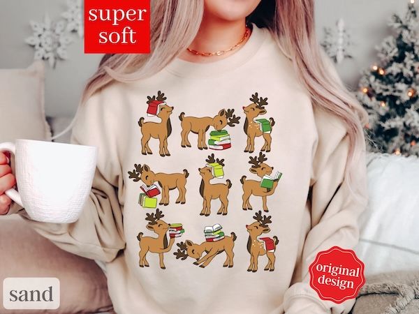 a white woman wearing a cream crewneck sweater with a graphic of nine reindeer, each posed differently with a small stack of books