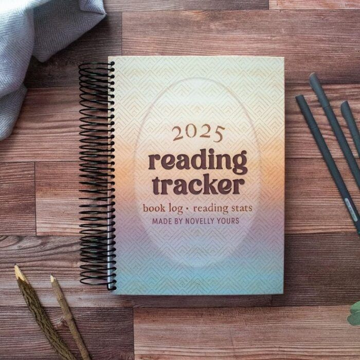 image of an ombre, spiral bound notebook with the title "2025 Reading Tracker" laying on a wooden table surrounded by pencils