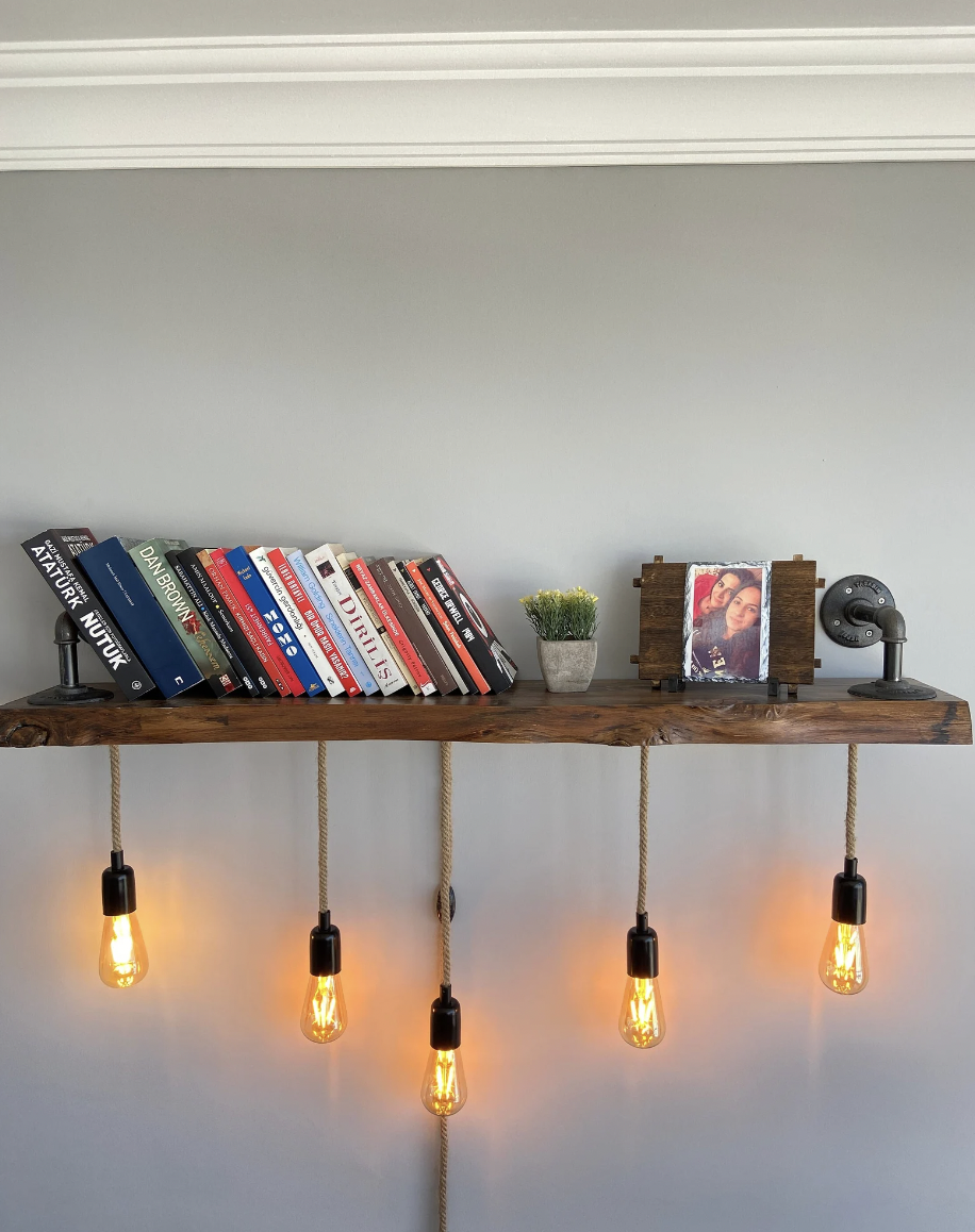 Photo of a wooden floating bookshelf high on a wall with hanging bulbs coming from the bottom side of the shelf