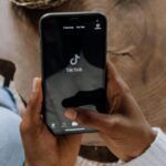 a brown-skinned hand opening up Tiktok on a smartphone