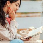 a light-tanned skin woman sitting on a bench and reading a book