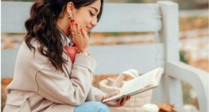 a light-tanned skin woman sitting on a bench and reading a book