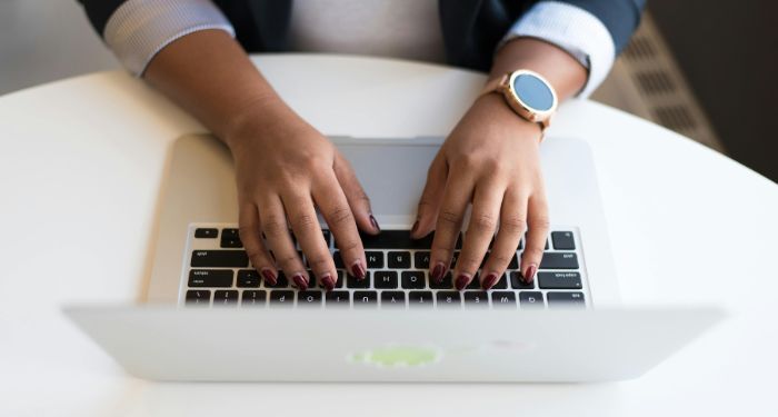 brown skinned hands with burgundy nails and a gold wrist watch typing on a mac keyboard.jpg.optimal