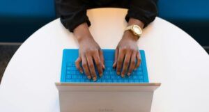 brown-skinned hands with gold wrist watch tying on a blue keyboard