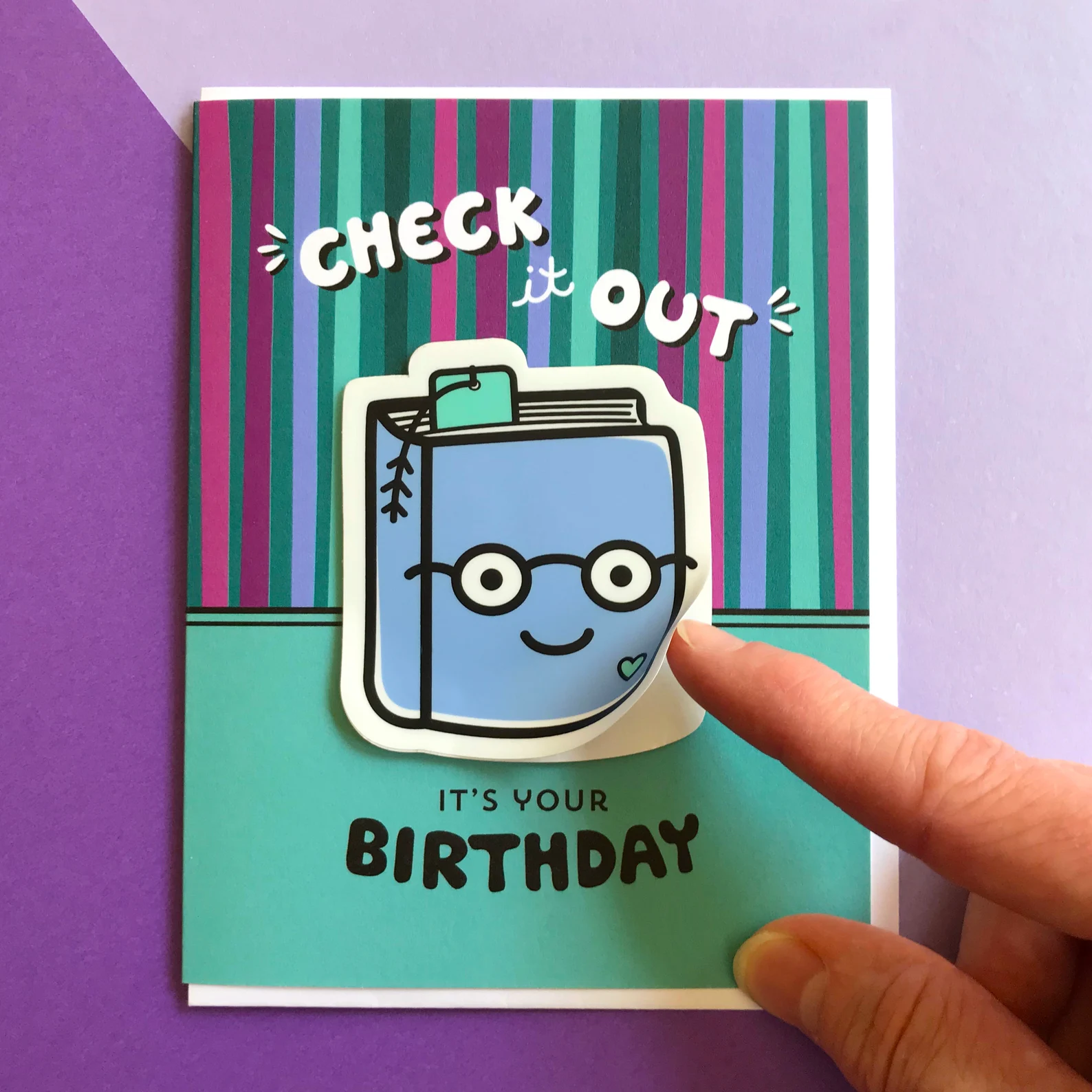 Image of a birthday card that says "check it out. it's your birthday." There is a book sticker on it. 