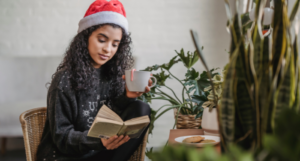 a woman with brown skin reading in a cafe while wearing a Santa hat