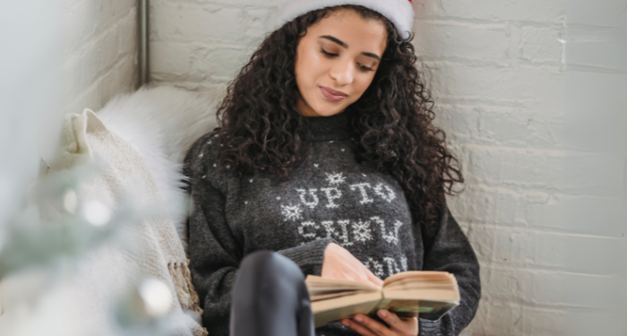 a woman with light brown skin and curly hair reading while wearing a Santa hat