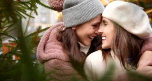 two women embracing closely in front of a christmas tree dressed for cold weather