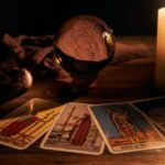 four tarot cards fanned out in front of a crystal ball and a lit candle on a wood surface in a dark room