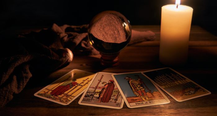 four tarot cards fanned out in front of a crystal ball and a lit candle on a wood surface in a dark room