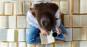 a young person with light skin and long brown hair reads on a floor of open books