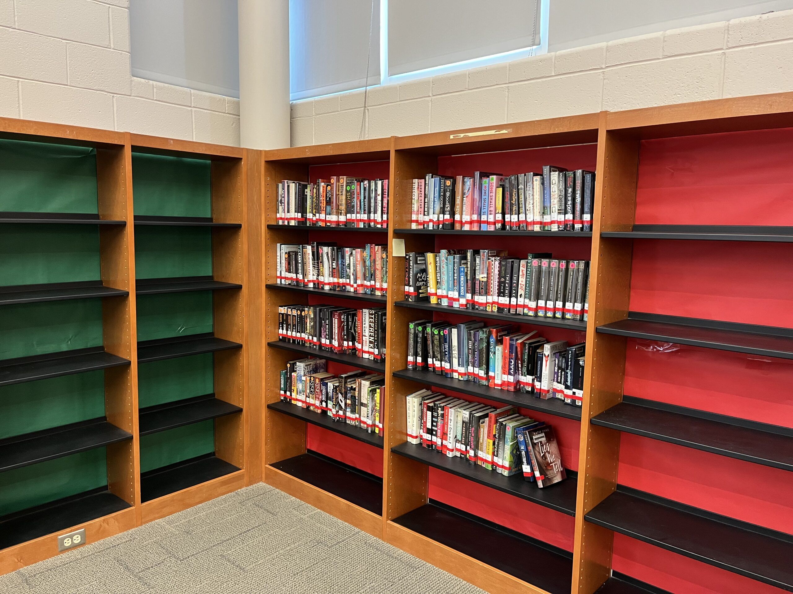 bookshelves with green and red paper backing, some shelves have books