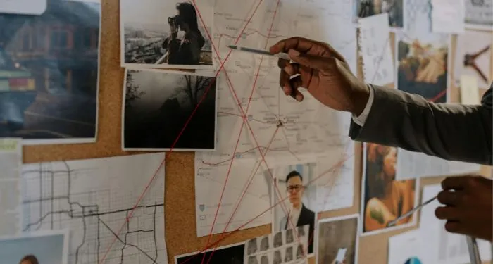 Investigation board with red string and images and a hand pointing with a pen
