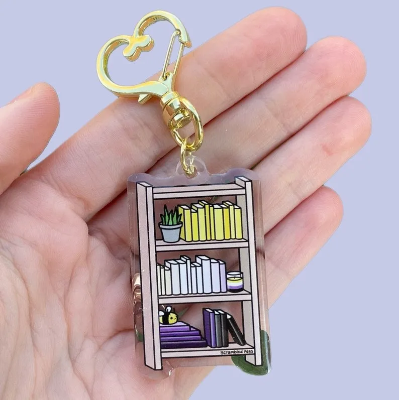 an acrylic charm keychain with a bookshelf in nonbinary pride flag colors