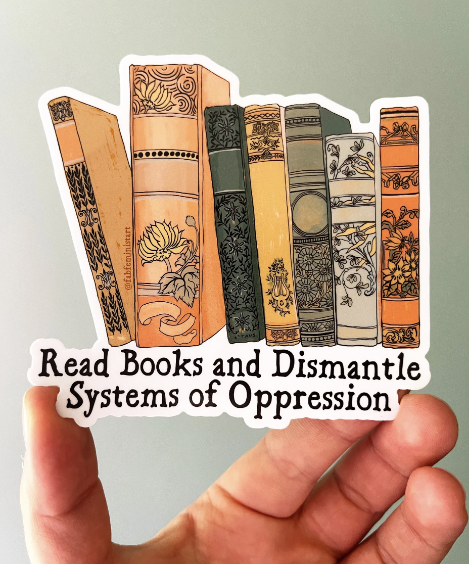 Photo of a hand holding a vinyl sticker with an illustration of book spines and the text "read books and dismantle systems of oppression"