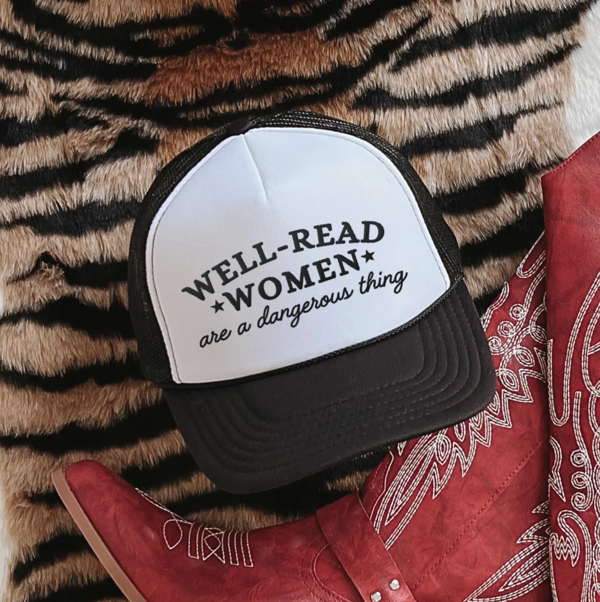 Image of a black and white trucker hat with the phrase "well-read women are a dangerous thing" on the front