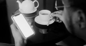 a brown-skinned person drinking tea and looking at their smartphone