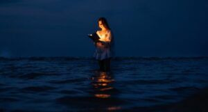 a fair-skinned young woman reading an illuminated book in the ocean