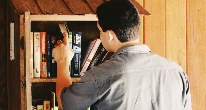 a light-medium skinned man looking at books in a Little Free Library