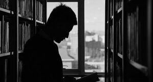 black and white photo of man reading a book in a library