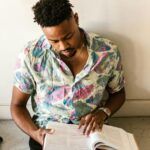 brown-skinned black man sitting on floor and reading, books surround him