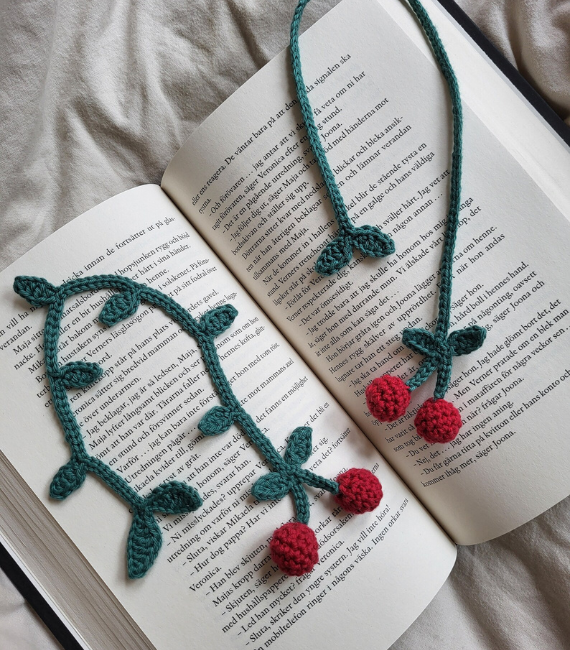 Two crocheted cherry bookmarks with green leaves spread out across an open book