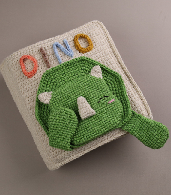 Crocheted quiet book featuring a green Triceratops on the cover and the word "DINO"