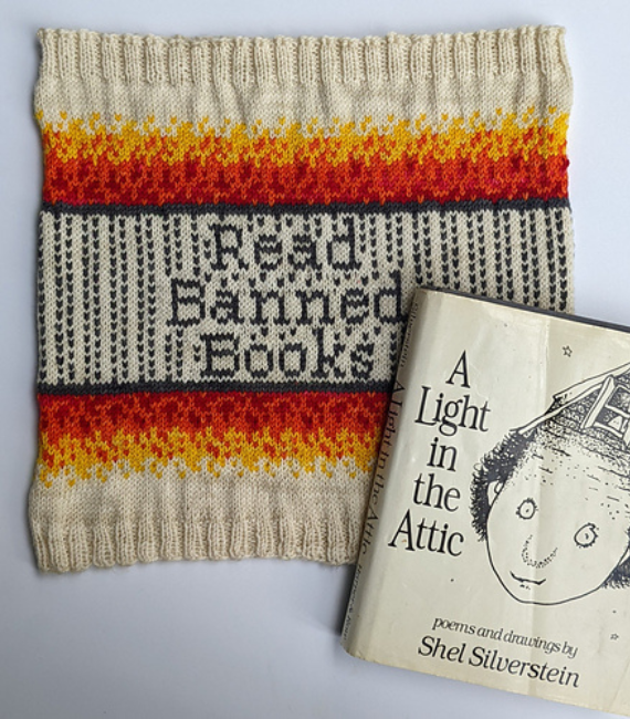 The book A Light in the Attic by Shel Silverstein sits next to a knitted cowl that reads "Read Banned Books" in black lettering surrounded by black stripes and flames