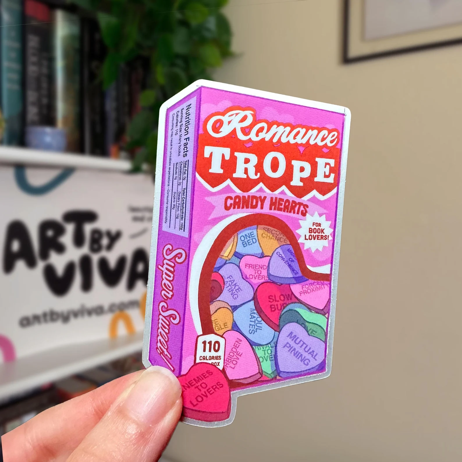 Image of a sticker in the shape of a candy hearts box. It says "Romance Trope Candy Hearts" and the images of candy hearts all have romance tropes. 