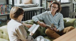 two people on a couch facing each other with open books