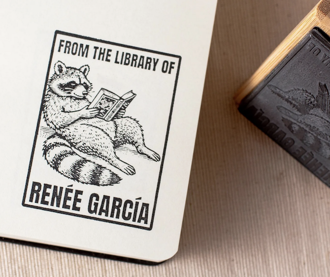 a custom ink stamp of a raccoon reading with text that says from the library of