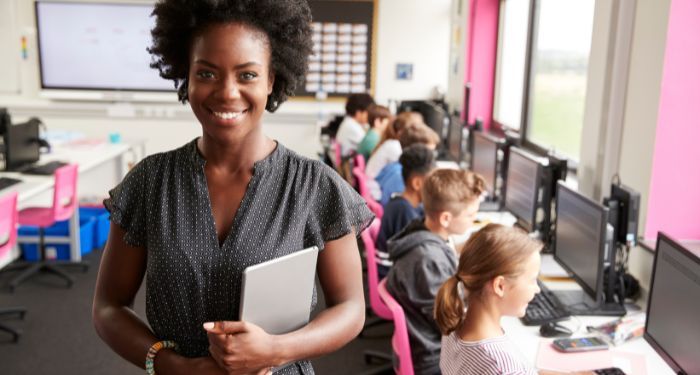 Image of a Black woman in front of a room of children on computers