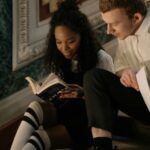 a brown-skinned Black woman and a fair-skinned white man sitting on stairs and reading a book