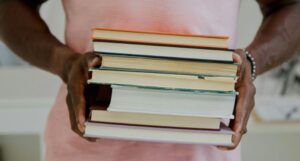 a dark brown-skinned man's hands holding a stack of books