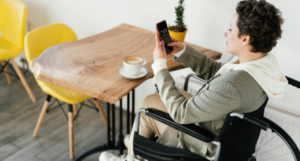 a fair-skinned, short-haired woman in a wheelchair looking at her phone in a cafe