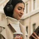 a light tan-skinned woman with a headscarf looking at her phone while wearing headphones