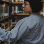 a plus sized fair skinned woman with short, dark hair looking at books on shelves