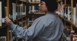 a plus sized fair skinned woman with short, dark hair looking at books on shelves