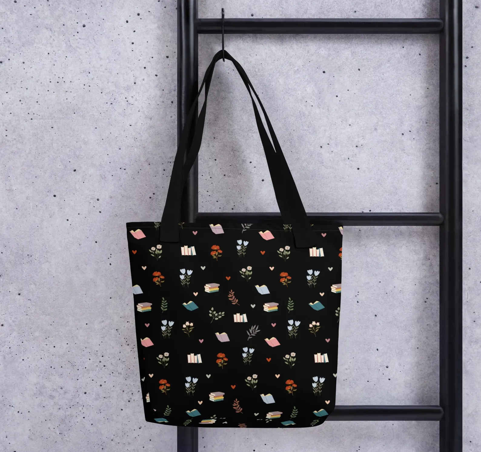 Image of a black tote bag. On it are small books, hearts, and flowers in various colors. 