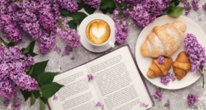 a book with lilacs, a latte, and croissants