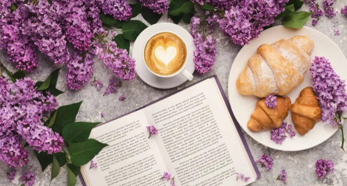 a book with lilacs, a latte, and croissants