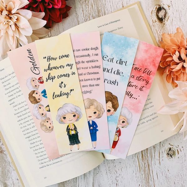 five Golden Girls-themed bookmarks fanned out in an open book. Each bookmark contains a quote from the show and an illustration of one or more of the four Golden Girls