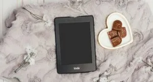 kindle on gray blanket with heart-shaped plate of chocolates nearby