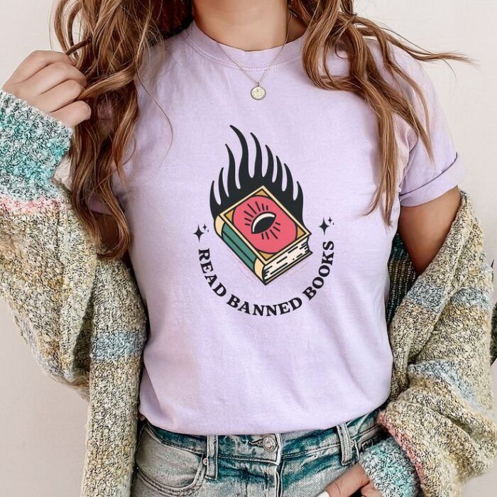 purple tshirt with a flaming book with an evil eye on the cover and the words 'read banned books.'