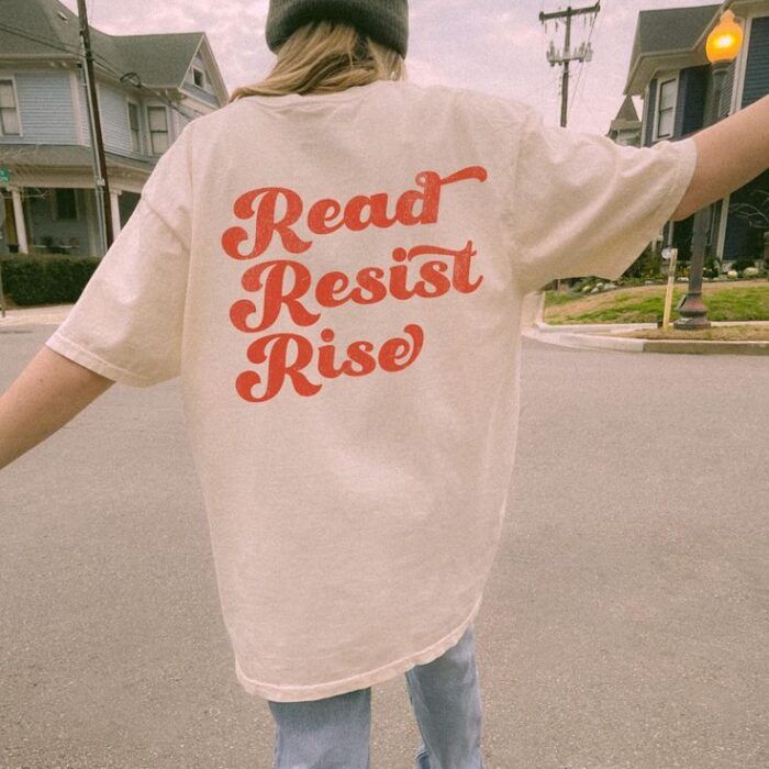 a pink shirt with red script that says "read, resist, rise"